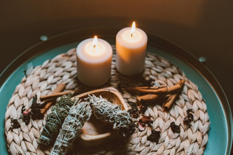 Warm and cozy candlelit setup featuring incense and herbs on a woven plate.