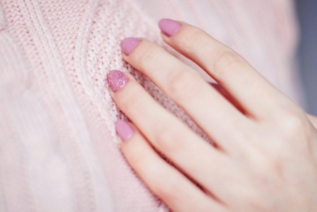 Close-up of a woman's hand with pink manicure resting on a soft knit sweater, showcasing elegance and fashion.
